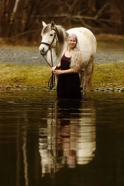 woman with white hairis in the water with white horse
