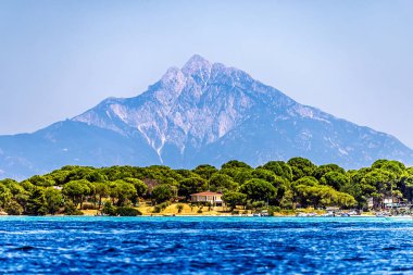 Asos Dağı 'nın parlak ve berrak manzarası yemyeşil kıyı ormanı ve bulutsuz gökyüzünün altındaki derin mavi denizin üzerinde yükseliyor..