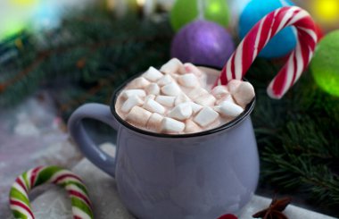 Yılbaşı kartı, marşmelovlu kakao, parıldayan çelenk, köknar dalları, gri arka planda koniler. Noel süsleri olan bir kartpostal.