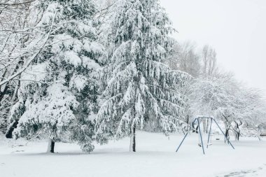Child swing set dusted with snow in a snow covered parkland during winter clipart