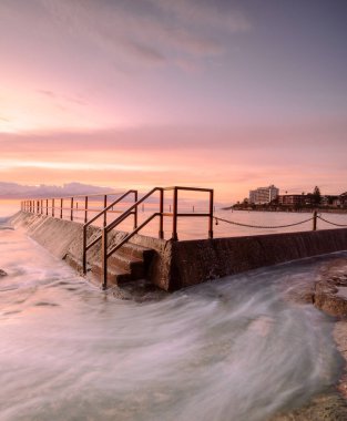 Cronulla Okyanusu 'nda gün doğumu. Okyanus etrafında dönüyor ve gökyüzü renkleri havuza yansıyor.