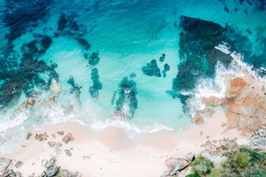 Sığ su, derin turkuaz sular, kayalar ve kum ile kumsalın havadan çekilmiş görüntüsü.