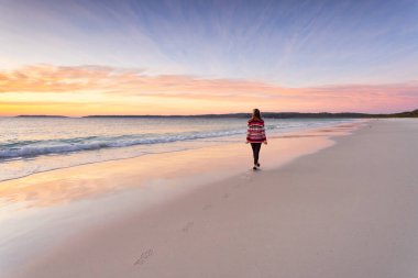 Woman daily morning walk along beach.  Sunrise sky and waves lapping on the shore. clipart