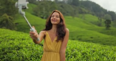 Selfie on smartphone of traveler woman during her travel vacation on famous nature landmark tea plantations in Sri Lanka. Fashion model vlogger outdoor photographing her self on cell phone camera