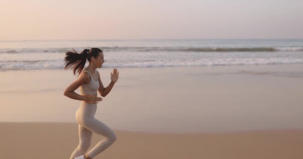 跑步的女人在户外运动中 女跑步者带着耳机在海滩上听音乐慢跑 漂亮的健身模特在户外 全长侧视图 高质量 慢投篮 — 图库视频影像
