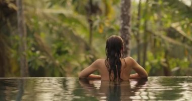 Genç yetişkin bir bikinili kadının, tropikal bir açık hava havuzunda lüks bir villada tropik bir tatil yaparken dinlenip vakit geçirmesi. Yüksek kalite 4K görüntü