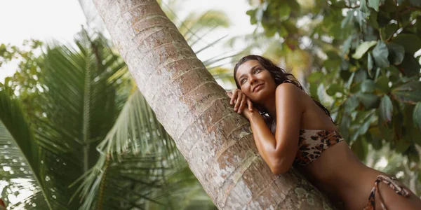 ファッショナブルなヒョウ柄のビキニを着た若い大人の女性が 熱帯雨林に幸せに横たわっています 彼女は夢のような週末の休暇を楽しんでいるので 彼女は気楽で幸せそうに見えます — ストック写真