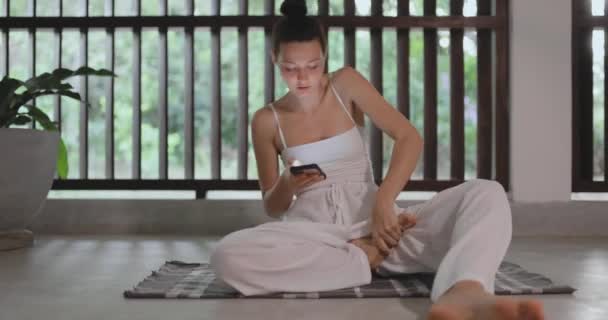 ヨガの教育の練習中に携帯電話を使用してヨガの初心者の女性は屋内 痛みを伴うポーズのために泣く若い大人の女性に合う 高品質4K映像 — ストック動画