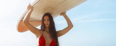 Plajda sörf tahtasını tutan genç bir sörfçü kadın portresi. Yüksek kaliteli fotoğraf.