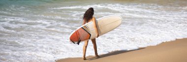 Sörfçü kız kumsalda sörf tahtasıyla yürüyor. Sahilde sörf tahtası olan güzel bir kadın. Yaz sporları, sörf. Yaz tatili. Yüksek kaliteli afiş fotoğrafı