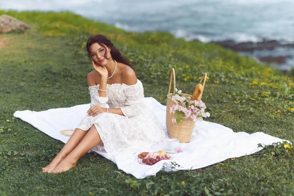 一位年轻的成年女子穿着一件浪漫的复古婚纱 在海滩上一边喝茶一边喝着羊角面包 享受着美妙的野餐 — 图库照片