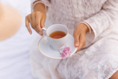 Bir kadın sıcak bir fincan çay tutarken dışarıda dinlenir, ferahlık ve rahatlama sağlar..