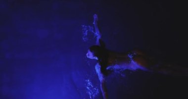 Siyah bikinili, kaplıca havuzunda dinlenen güzel, yetişkin, seksi Asyalı bir kadın. Mükemmel vücutlu, geceleri yüzen modaya uygun bir model. Sinema yaratıcı ağır çekim 4k görüntü.