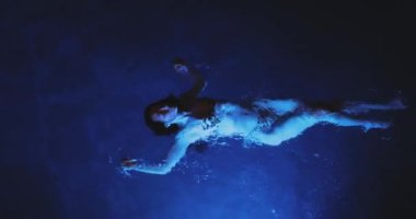 Siyah bikinili, kaplıca havuzunda dinlenen güzel, yetişkin, seksi Asyalı bir kadın. Mükemmel vücutlu, geceleri yüzen modaya uygun bir model. Sinema yaratıcı ağır çekim 4k görüntü.