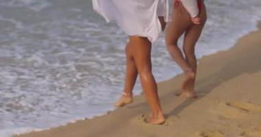 İki genç kadın, bikinili mankenler, güneşli bir sahilde birlikte koşuyorlar, arkadaşlığın ve özgürlüğün kaygısız yaz günlerinin tadını çıkarıyorlar.