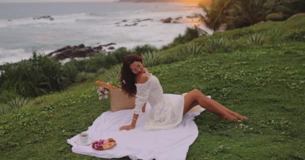 日落时在海边吃浪漫的野餐晚餐 女人一个人坐在那里 等着她的男朋友为她一顿浪漫的晚餐 海滩的天空和大海的背景音乐 在户外为一对恋人共进晚餐 — 图库视频影像