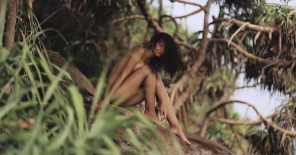 野生の岩の海岸に完全に日焼けした体を持つ魅力的な若い女性 スリムな女の子は完全に裸で海に向かって岩の上に座って サイドビュー 高品質のファインアートスローモーション映像 — ストック動画