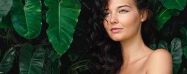 Ormanda egzotik bitkilerin arasında duran mükemmel ciltli, doğal makyajlı ve sağlıklı saçlı esmer bir kızın güzellik spa portresi. Yüksek kaliteli cilt bakımı ve doğal kozmetik konsept fotoğraf