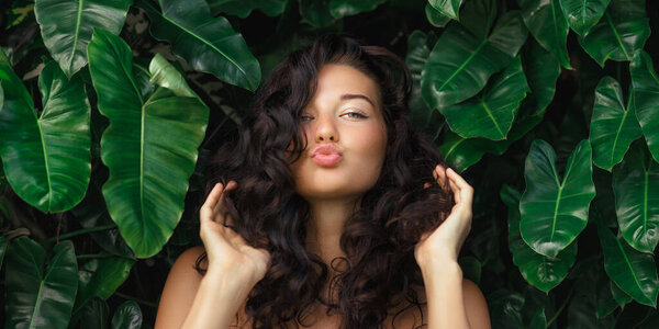 Косметика и уход за кожей. Портрет красивой женщины морщинистые губы, поцелуи, показывая естественную чистую кожу лица, стоя над тропической листвы стены. Высокое качество баннерного фото