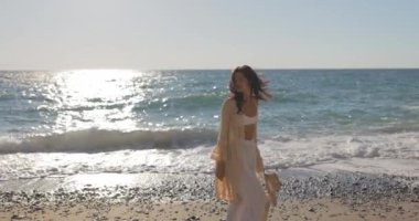 Ağır çekimde, sahilde yürüyen genç Asyalı kadın. Güzel dişiler, akşam günbatımında deniz kenarında yürürken mutlu mesut dinlenirler. Hayat tarzı kadınlar plaj konseptiyle seyahat eder. Yüksek kalite 4k görüntü