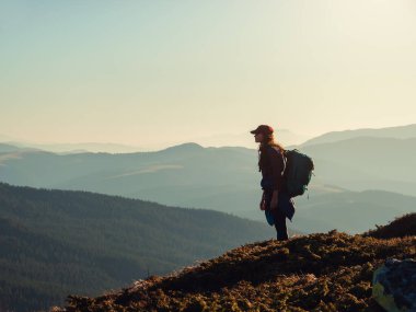 Sırt çantasıyla dağın tepesinde rahatlayan ve vadi manzarasının tadını çıkaran yürüyüşçü kadın silueti. Turizm ve seyahat kavramı
