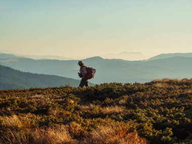 Dağ yürüyüşü sırasında sırt çantalı bir turist. Arka planda akşam dağlarının görkemli manzarası.