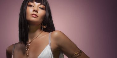 Queen Cleopatra stüdyo güzellik portresi. Mükemmel makyajlı, düzgün saç kesimi peruklu, pembe arka planda altın takılar takan genç bir moda kadını. Yüksek kalite