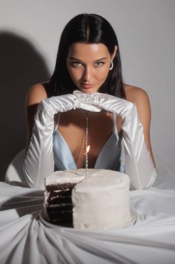 Doğum günü pastasının önünde mavi ipek bir elbise giymiş, kameraya bakan bir mumla göz kamaştırıcı, şık, lüks bir kız. Moda ve güzellik makyajı veya kozmetik