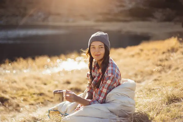 美丽的女旅行家带着一杯饮料在湖边远足 露营旅行的理念 正在度假欣赏大自然美景的女孩 图库图片