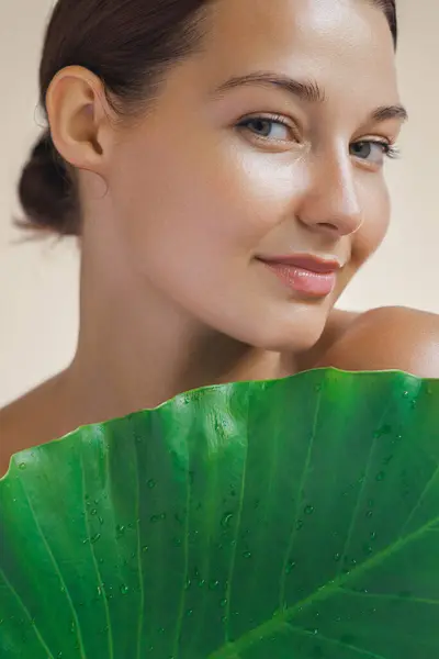 天然化粧品スキンケアビューティープロダクト 大きな熱帯緑の葉で彼女の体を覆う美しい顔と健康な顔の肌を持つ女性 ストックフォト