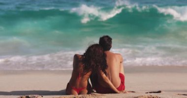Erkek ve kadın kumlu bir sahilde okyanusun kenarında otururken konuşuyor. Esmer, beyaz bir kadın ve bir adam sırtı kameraya dönük dalgalara bakıyor. Romantik kavram.