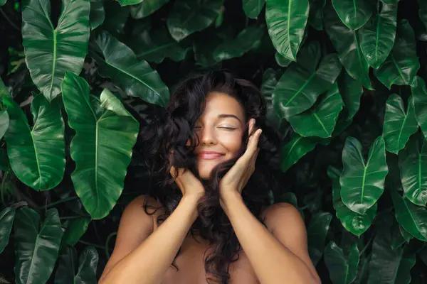 エキゾチックな植物の間でジャングルの前に彼女の健康な光沢のある髪に触れる完璧な肌 自然なメイクアップの若いブルネットの自然なヘアケアの肖像画 高品質の髪天然化粧品写真 ストック写真