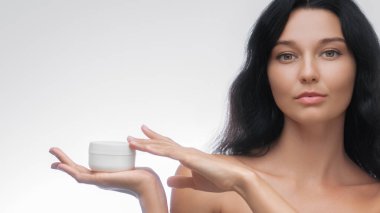 Parlak stüdyo arka planında izole edilmiş güzellik ürünlerini gösterirken gülümseyen üstsüz bir kadının güzellik ve cilt portresi. Yüksek kaliteli afiş fotoğrafı