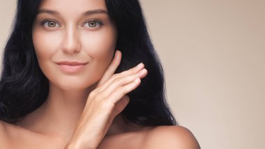 Mutlu, güzel, genç bir kadın, mükemmel yüzüne dokunuyor, sağlıklı, parlak teniyle, el ele. Bej arka planda sabah güzelliğinden sonra güzel bir kızın güzel afiş fotoğrafı.