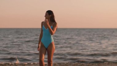 Yüksek kalite plaj seyahat videosu. Açık mavi mayo giymiş bir kadın gün batımında sahilde poz veriyor, deniz kenarında huzurlu ve güzel bir akşamın tadını çıkarıyor. Sinema yavaş çekim 4k görüntü, için tasarım