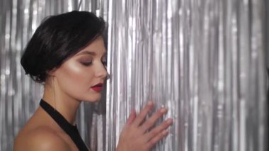 Kısa siyah saçlı, kırmızı rujlu, siyah kolsuz bluzlu, siyah flama üzerine poz veren zarif bir kadın, kendinden emin bir şekilde uzaklaşıyor. 