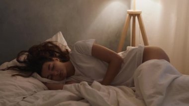 Bir kadın geceleri yatağında huzur içinde uyur. Dinlenme, rahatlama ve huzurlu bir uyku ortamı sunar..