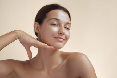 Metin için fotokopi alanı olan yüksek kaliteli cilt bakımı ve kozmetik konsepti. Işıl ışıl parlayan cildi olan doğal güzel bir kadın gözlerini kapatır ve eliyle nazikçe yüzüne dokunur.