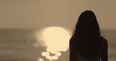 Sakin bir okyanusta gün batımını izleyen bir kadının kavramsal fotoğrafı. Seyahat blogları, rahatlama temaları ve doğa için ideal..