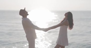 Gün batımında deniz kenarında el ele tutuşan mutlu bir çift. Romantizm, mutluluk ve aşk kavramları için mükemmel, reklamlar ve seyahat promosyonları için ideal.. 