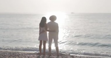 Sahilde kol kola duran bir çiftin okyanusta gün batımını izlediği romantik bir sahne. Bu kaliteli stok fotoğrafı aşk, romantizm ve huzurlu anlar için mükemmeldir.
