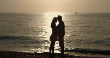 Gün batımında sahilde öpüşen bir çiftin romantik silueti. Arka planda okyanus var. Bu yüksek kaliteli fotoğraf aşk, romantizm ve deniz kenarındaki huzurlu anları yakalıyor.