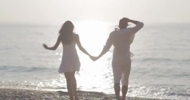 Gün batımında kumsalda el ele koşan mutlu bir çift. Aşk, mutluluk ve kaygısız anlar için mükemmel. Seyahat ve yaşam tarzı reklamları için ideal.. 