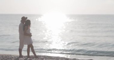 Gün batımında sahilde kucaklaşan romantik bir çift, arka planda bir tekne. Aşk, romantizm ve huzurlu anlar için mükemmel. Seyahat ve yaşam tarzı reklamları için ideal.. 