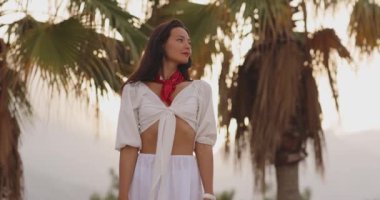 Beyaz elbiseli, kırmızı eşarplı ve tropikal tatilin tadını çıkaran şık bir kadının yüksek kalite görüntüleri. Seyahat blogları, moda promosyonları ve yaşam tarzı içeriği için mükemmel.