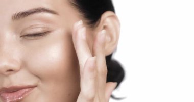 Cilt bakımının yüksek kaliteli yavaş çekim videosu ve metin için fotokopi alanı ile kozmetik konsepti. Güzel yüzlü bir kadın sağlıklı yüz portresine dokunuyor. Güzel mutlu Asyalı kız modeli