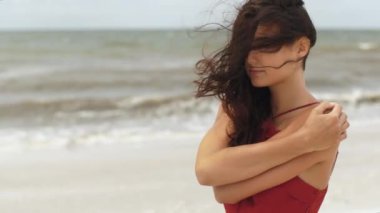 Kırmızı elbiseli düşünceli bir kadın rüzgarlı bir sahilde kendini kucaklıyor, düşüncelere dalmış. Yalnızlık, tefekkür ve seyahat, moda ve yaşam tarzında içgözlem kavramları için mükemmel.