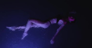 Sakin, genç bir kadın geceleri yüzme havuzunda dinleniyor, yukarıdan manzara seyrediyor. Yüksek kalite ağır çekim 4k görüntü. 