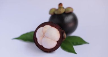 Beyaz tenli, bütün ve yarı yarıya mangosteen, beyaz bir yüzeyde yeşil yapraklar eşliğinde. Tropikal meyve reklamları, sağlıklı beslenme görselleri ve mutfak kavramları için mükemmel.. 