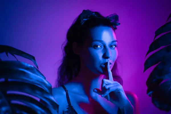 stock image A stunning model with cat ears and lingerie makes a shushing gesture in neon lights, creating a mysterious and seductive atmosphere. Perfect for themes of secrecy, fetish, and party allure in